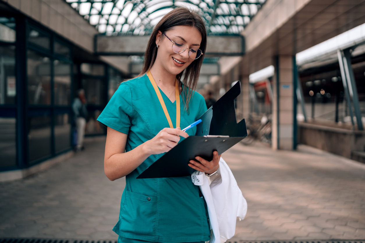 A person in a green scrubs writing on a clipboard Description automatically generated