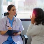 A doctor writing on a clipboard next to a person Description automatically generated