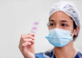 A person wearing a mask and holding a test tube Description automatically generated