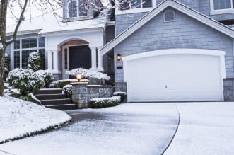photo of suburban home with snow on drive way, lawn, plants, trees and roof