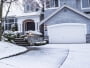 photo of suburban home with snow on drive way, lawn, plants, trees and roof
