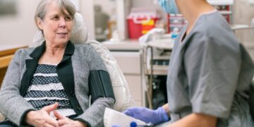 A person sitting in a chair with a nurse in the background Description automatically generated with low confidence
